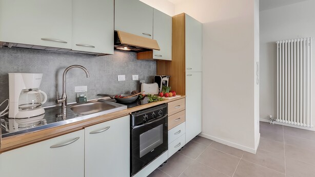 A modern kitchen with light-colored cabinets, a stainless steel sink, a coffee maker, and a built-in oven. - Appartamento 30 Nodi 2 Torbole-arco (Arco)