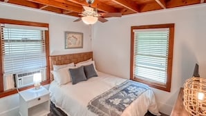 A bedroom with a wooden ceiling, a bed with a white comforter, two bedside tables, and a nightstand.