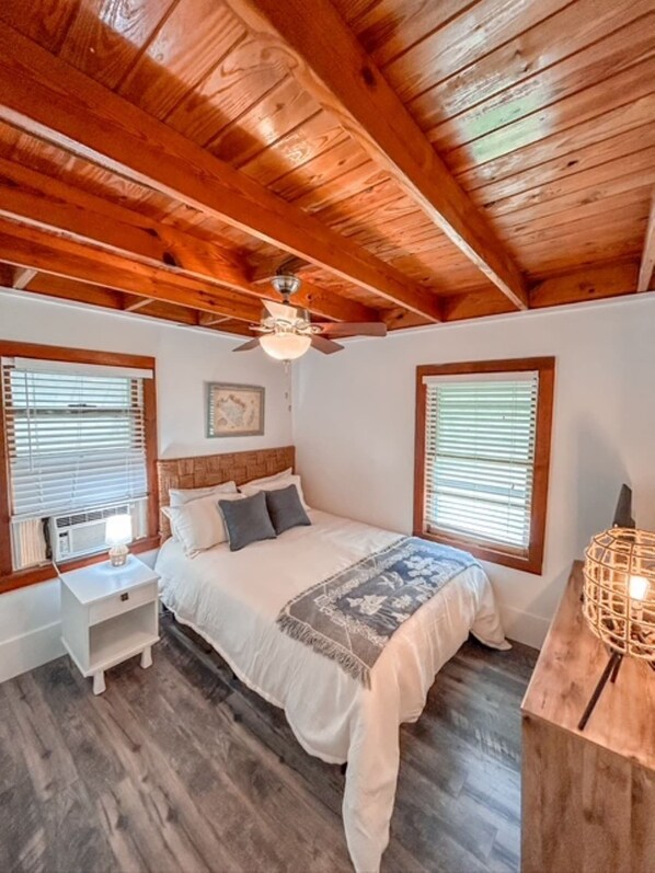 A bedroom with a wooden ceiling, a bed with a white comforter, two bedside tables, and a nightstand. - Sammie's Retreat (Carolina Beach)