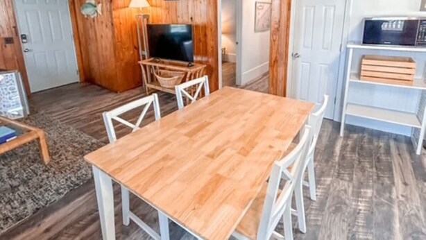 A wooden interior with a dining table and chairs, a television, and a shelf with items.