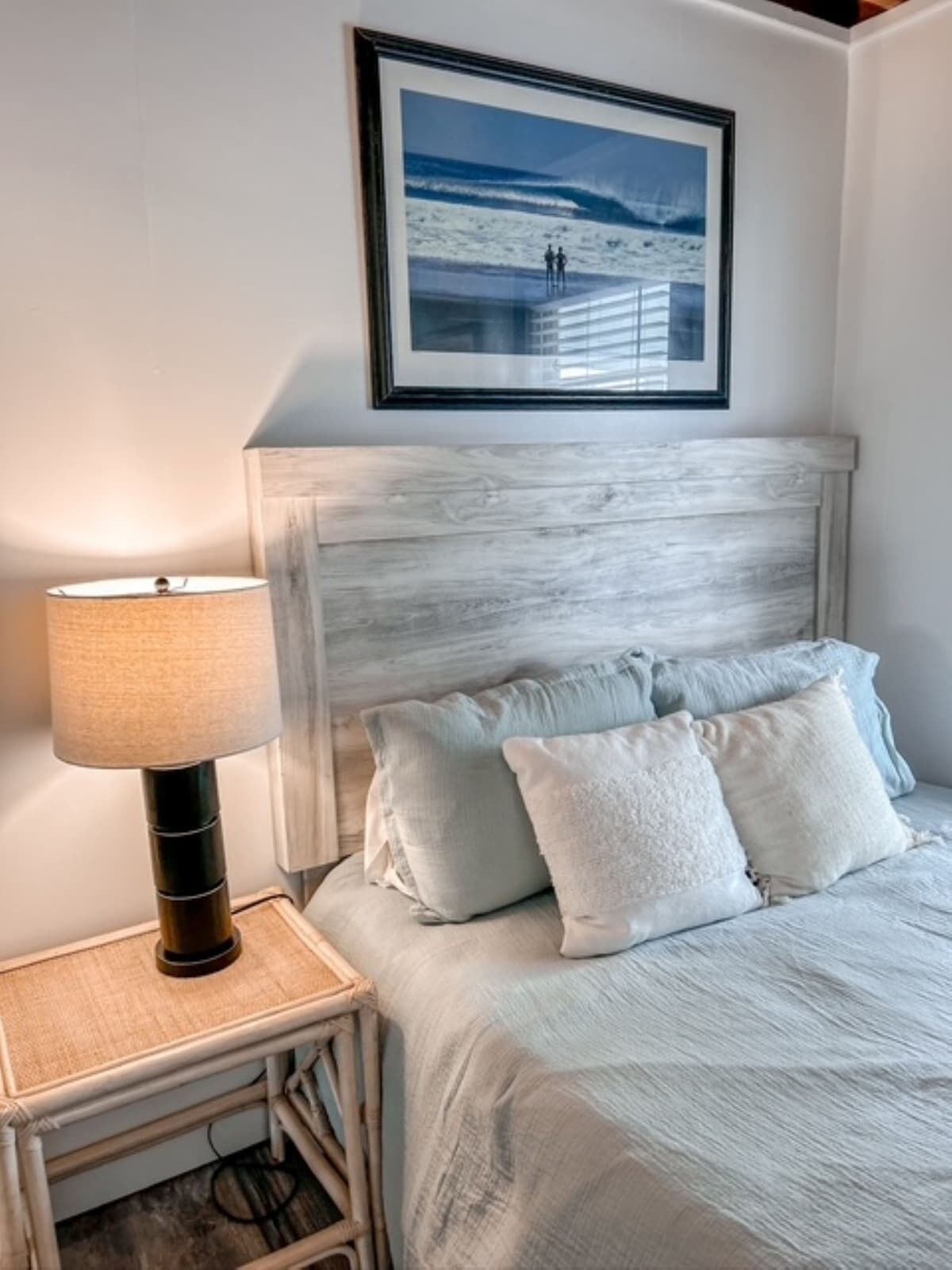 Un dormitorio con cama, mesita de noche, lámpara y un cuadro en la pared.