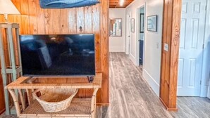 A wooden interior with a TV on a stand, a woven basket, and a hallway leading to a door.