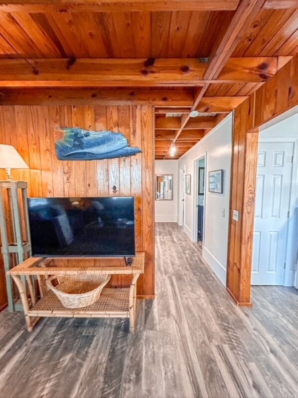 A wooden interior with a TV on a stand, a woven basket, and a hallway leading to a door. - Sammie's Retreat (Carolina Beach)