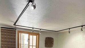 Ein Wohnzimmer mit braunem Ledersofa, einem Couchtisch aus Holz, einem gemusterten Teppich, einem Fenster mit Jalousien und einem Wandbild.
