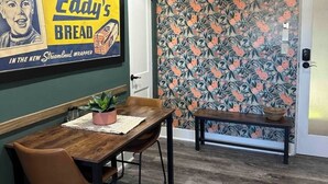 Ein Essbereich mit Holztisch und -stühlen, einem Blumentopf und einer Wand mit einem Vintage-Poster.