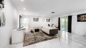 A modern living room with a white sofa, a coffee table, and artwork on the walls. - Delray Beach Home w/ Pool ~ 4 Mi to Beach! (Delray Beach)