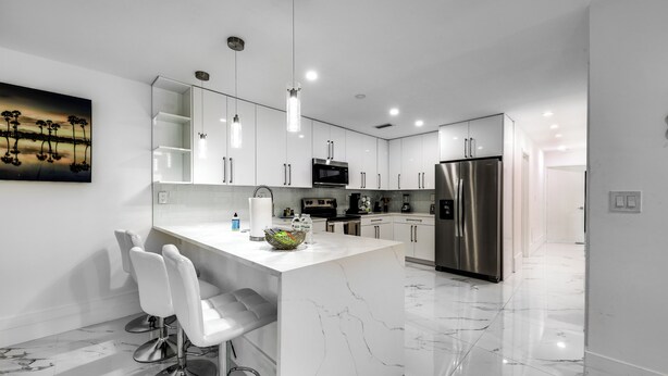 A modern kitchen with white cabinets, stainless steel appliances, and a marble island with bar stools. - Delray Beach Home w/ Pool ~ 4 Mi to Beach! (Delray Beach)