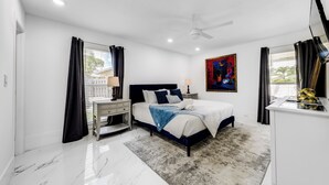 A modern bedroom with a bed, bedside tables, a desk, a ceiling fan, and a painting on the wall. - Delray Beach Home w/ Pool ~ 4 Mi to Beach! (Delray Beach)