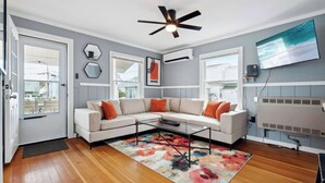 Una sala de estar moderna con un sofá modular, un ventilador de techo y un ventanal grande.