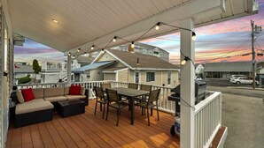 Una terraza cubierta al aire libre con sofá, mesa de comedor y sillas, con vista a una calle con casas y coches.