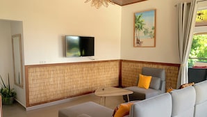 A modern living room with a sofa, a small table, a TV mounted on the wall, and a painting of a beach scene.