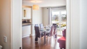 A modern kitchen with white cabinets, a microwave, and a dining area with a glass table and chairs. - Carraroe Apartment ideal base to tour Connemara (Carraroe)