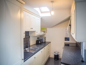 A compact kitchen with white cabinets, a black countertop, a toaster, and a sink. - Carraroe Apartment (Carraroe)