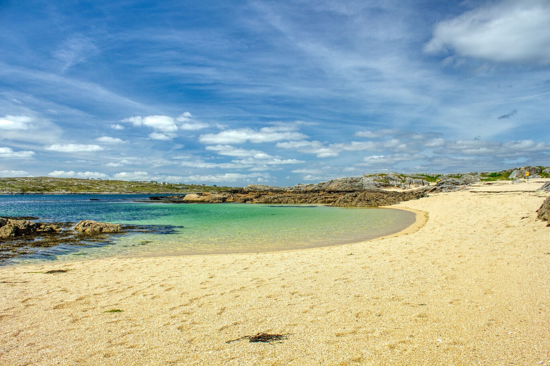 Una playa con agua cristalina, orilla arenosa y afloramientos rocosos.