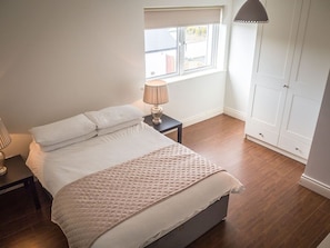 Une chambre à coucher avec un lit, une table de chevet, une lampe, une fenêtre et une armoire.