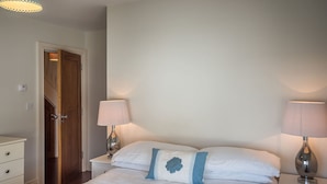 A bedroom with a bed, two bedside lamps, a nightstand, a dresser, and a door. - Carraroe Apartment ideal base to tour Connemara (Carraroe)