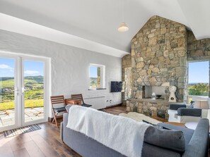 A spacious living area with a stone fireplace, a sofa, and a television. - Paddy Carroll´s, Ballyconneely (Ballyconneely)