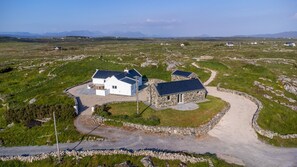 Il s’agit d’une propriété rurale comprenant deux bâtiments principaux : une construction en pierre et une maison blanche, le tout entouré d’une allée gravillonnée et de champs verdoyants.