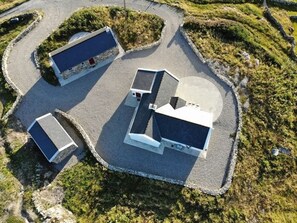 A building with a flat roof, surrounded by a paved area and vegetation. - Paddy Carroll´s, Ballyconneely (Ballyconneely)