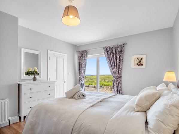 A bedroom with a large bed, a dresser, a mirror, and a window with curtains. - Paddy Carroll´s, Ballyconneely (Ballyconneely)