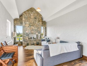 Un salon chaleureux avec une cheminée en pierre, un canapé gris, des meubles en bois et une vue par la fenêtre.