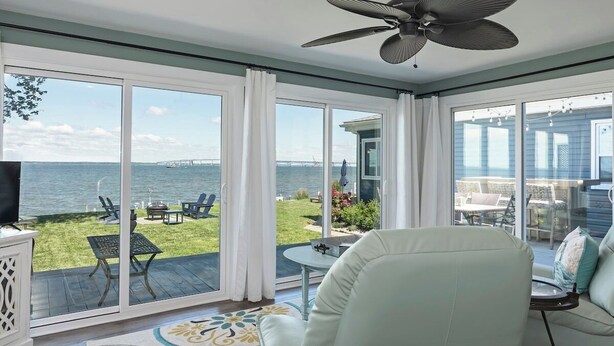 A spacious room with a large sliding glass door leading to a deck with outdoor furniture and a view of the water.