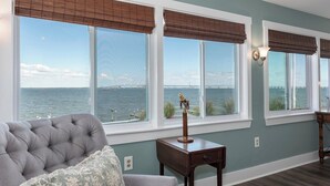 A living room with a view of the water, a tufted sofa, and a small table with a lamp.