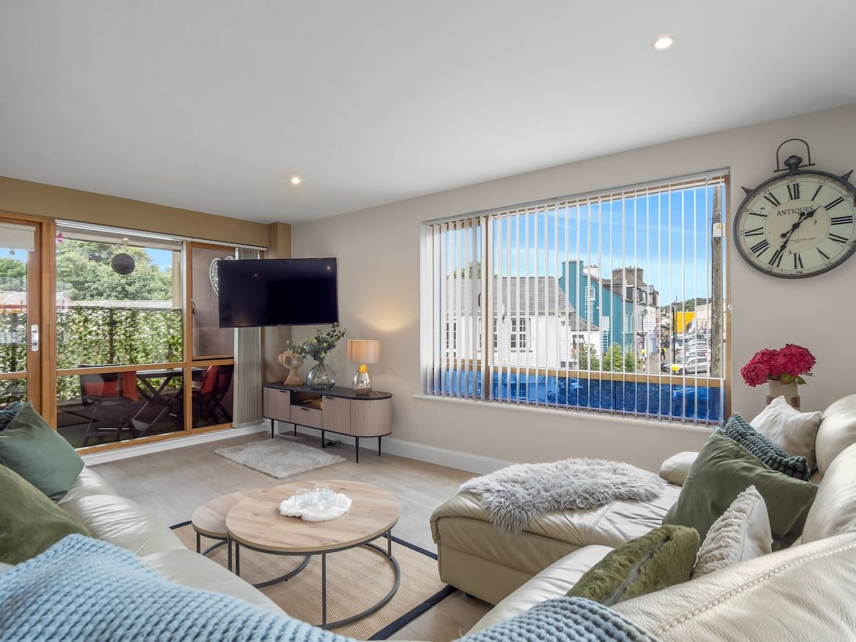 A modern living room with a sofa, a coffee table, a TV, and a large window with blinds.