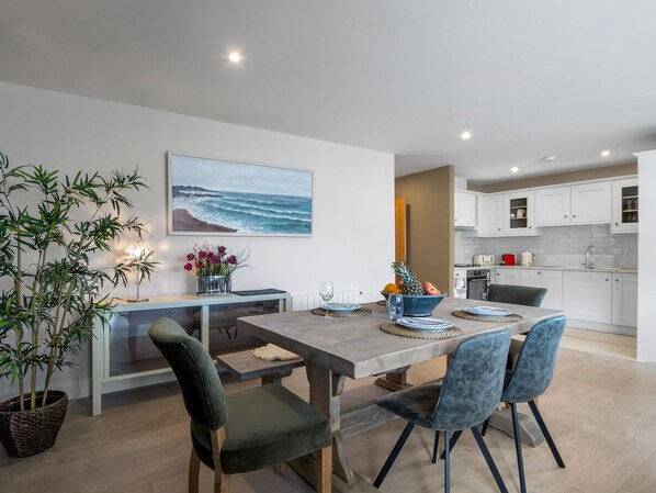 A modern kitchen with white cabinets, a dining area with a wooden table and chairs, and a large painting of a beach scene.