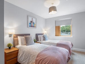 A modern bedroom with two beds, a bedside table with a lamp, a wall-mounted artwork, and a window with a view. - Robins Nest (Clifden)