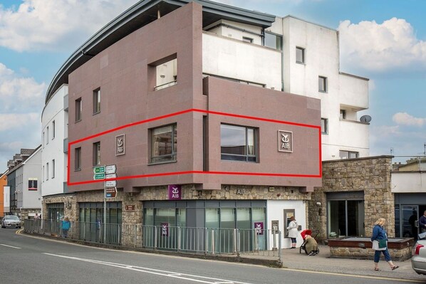 A multi-story building with a flat roof, a red outline marking a section, and a sign indicating a business or service on the ground floor. - Robins Nest (Clifden)