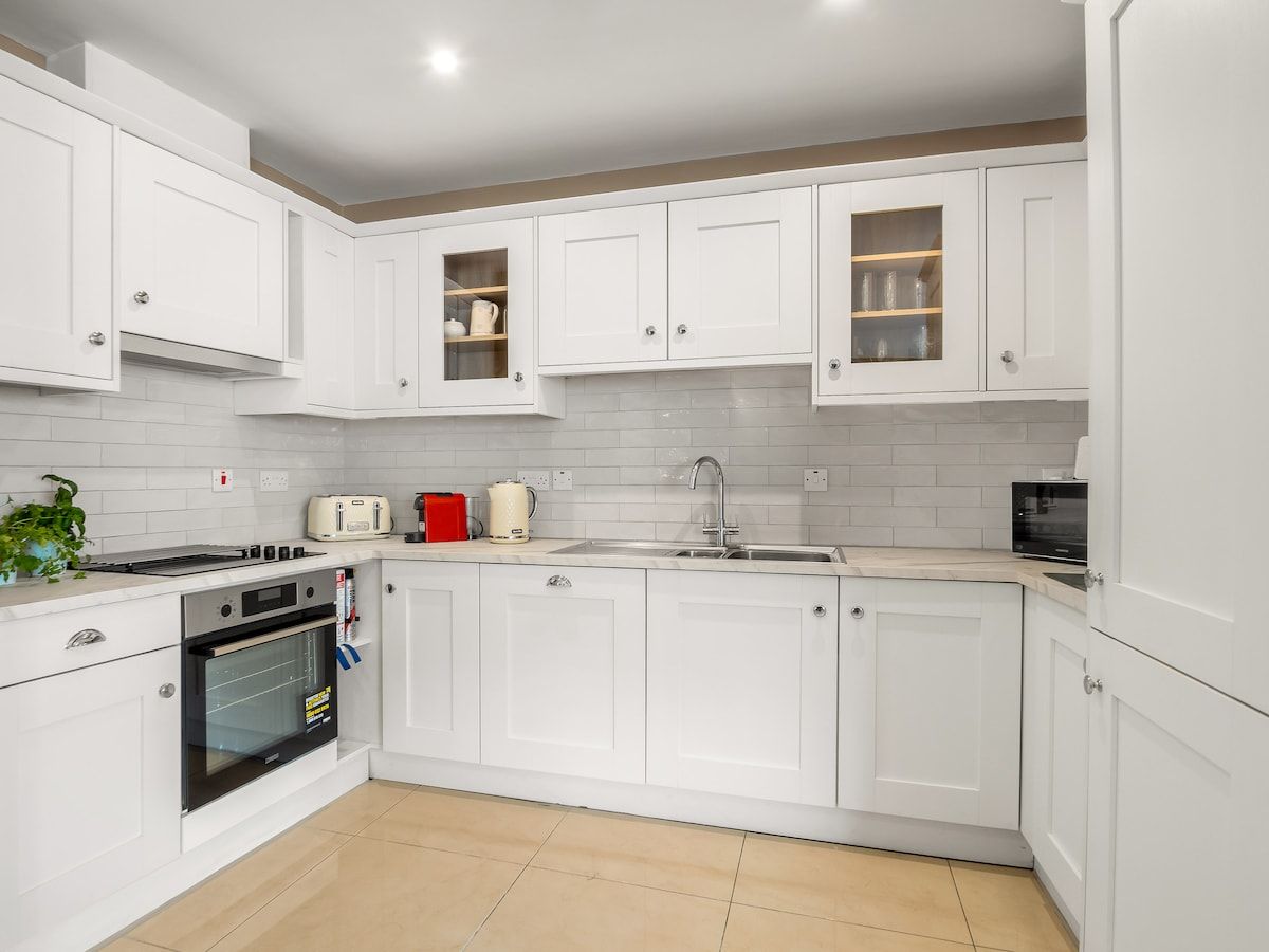 A modern kitchen with white cabinetry, a built-in oven, a microwave, and a sink.