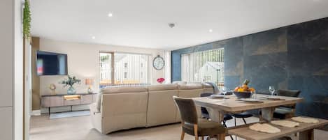A modern living space with a dining area, a sofa, and a kitchen in the background.