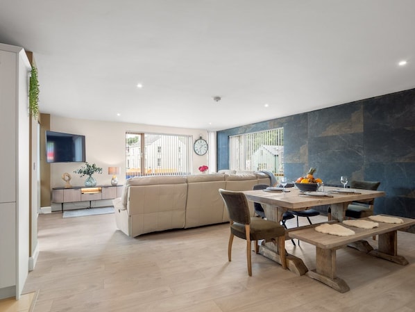A modern living space with a dining area, a sofa, and a kitchen in the background.