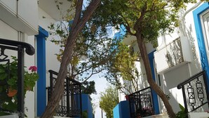 A narrow street with white and blue buildings, a tree, and a red car in the distance.