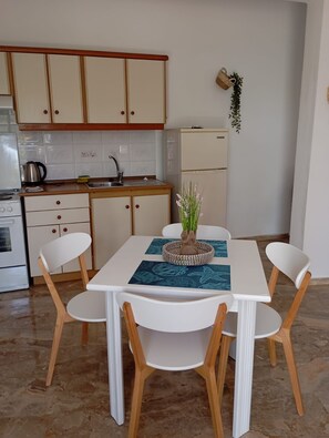Cocina compacta con armarios blancos, refrigerador y una mesa de comedor con sillas.
