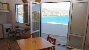 Una habitación con mesa de madera, sillas, una pequeña cocina y un cristalero corredizo que da a un balcón con vista al mar.