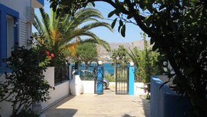 Un sendero estrecho que conduce a una entrada con puerta, donde se ve un vehículo estacionado, rodeado de vegetación y con vista despejada al mar.