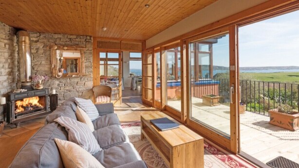 Een ruime woonkamer met een open haard, een grote bank en een balkon met uitzicht op het landschap.