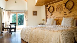 Een slaapkamer met een groot bed, een houten hoofdbord en uitzicht op de omgeving door een glazen deur.