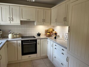 Una cocina con armarios blancos, un horno negro y una encimera con varios objetos.