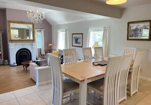 Un coin repas avec une table en bois et des chaises blanches, une cheminée et un lustre.