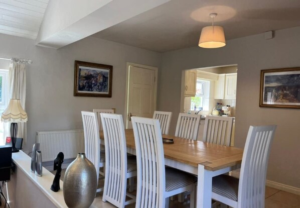 A dining area with a wooden table and white chairs, a pendant light, and artwork on the walls. - River Cottage (Clifden)