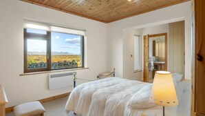 Un dormitorio con un ventanal grande, una cama, una mesita de noche y una lámpara.