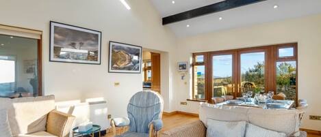 A spacious living room with a high ceiling, large windows, and a dining area.