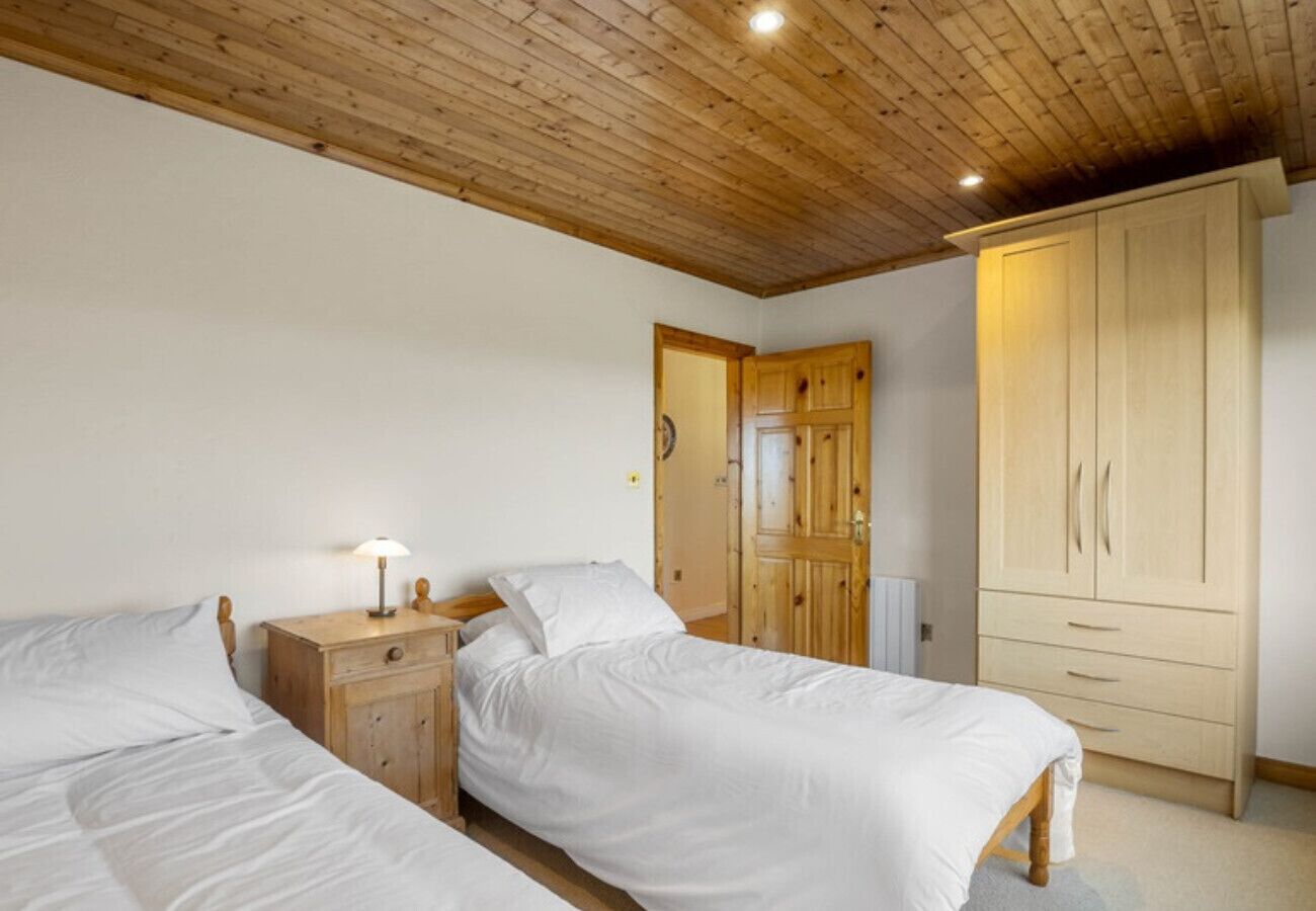 Une chambre avec deux lits simples, des tables de chevet en bois, une armoire et un plafond en bois.