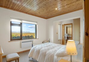 A bedroom with a large bed, a window with a view, a radiator, and a lamp.