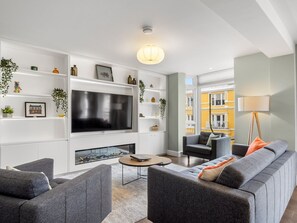 A modern living room with a flat-screen TV, grey sofas, a coffee table, and a fireplace.