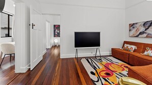 Ett modernt vardagsrum med en platt-TV på ett TV-bord, en soffa, en mönstrad matta och en tavla på väggen.