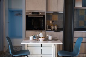A modern kitchen with a white countertop, two blue chairs, a white table, and a built-in oven.